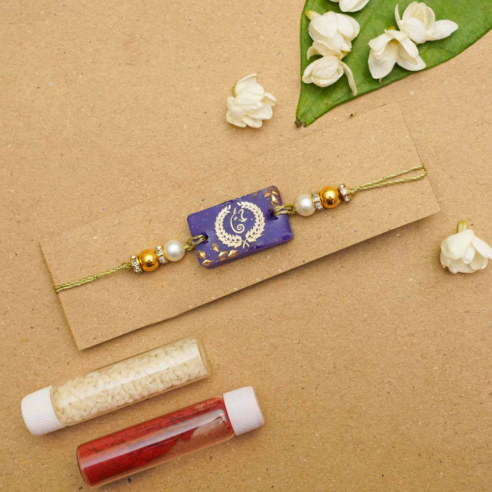 Handmade Resin Plural Ganesha Rakhi With Roli Chawal - Flat lay with decorative powders