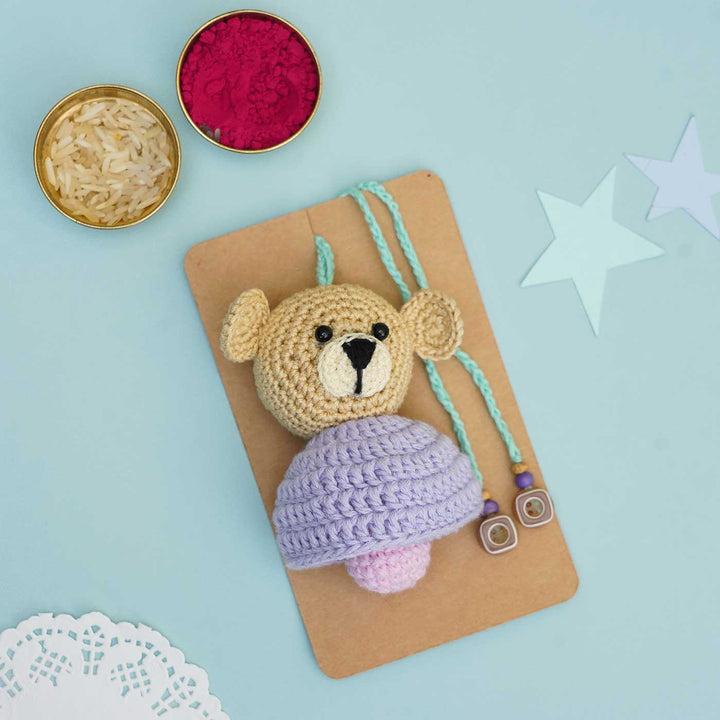 Handmade Crochet Teddy Hug Kids Rakhi With Roli Chawal - Flat Lay Front View with Purple Cap
