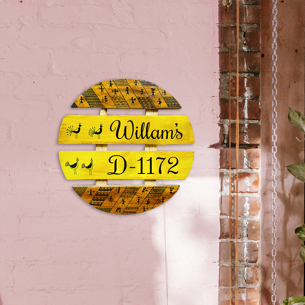 Handcrafted Personalized Warli Art Round Pinewood Name Plate - Mounted on Pink Wall Front View