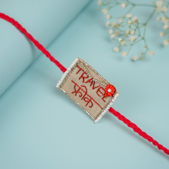 Handmade Beaded Travel Freak Rakhi With Roli Chawal For Brother - Angled view of Rakhi on blue background
