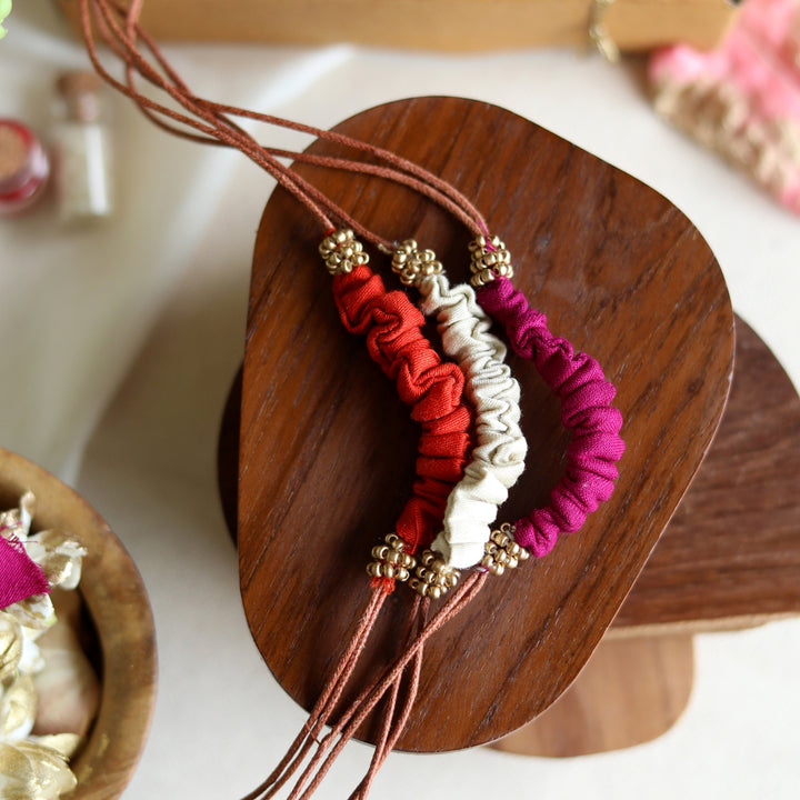 Handmade Reusable Beaded Ruched Upcycled Fabric Rakhi With Roli Chawal For Brother Set Of 3 - Close-up of bracelets on wooden stand