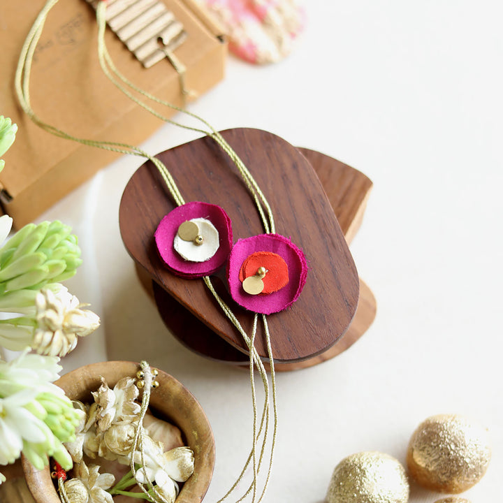 Handmade Reusable Floral And Gold Accent Upcycled Fabric Rakhi With Roli Chawal For Brother Set Of 2 - Styled on wooden display with alternate colors
