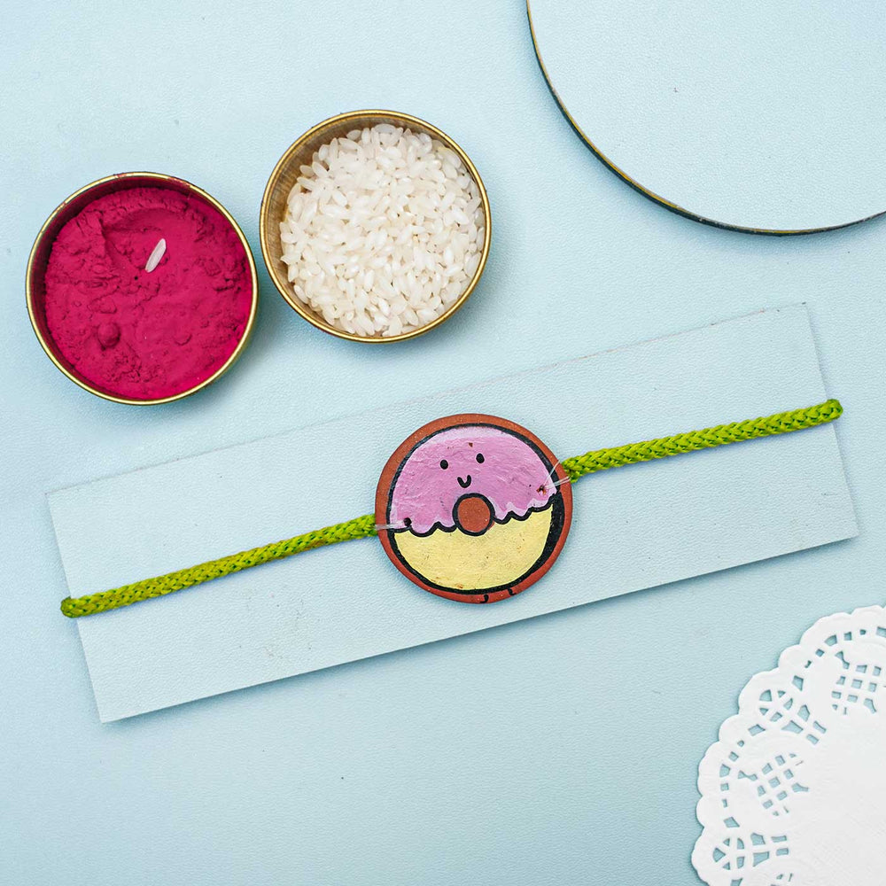 Hand Painted Donut Theme Terracotta Rakhi With Roli Chawal - Flat Lay with Rakhi and Accessories