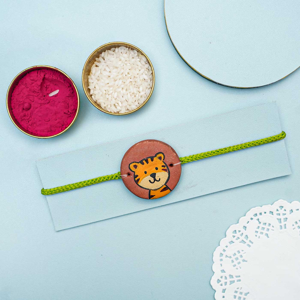 Hand Painted Tiger Terracotta Rakhi With Roli Chawal For Kids - Full View with Decorative Items