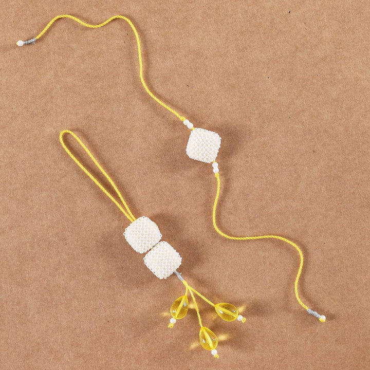 Handmade Square Pearls Bhaiya Bhabhi Rakhi With Roli Chawal Set Of 2 - Flat Lay on Plain Brown Background