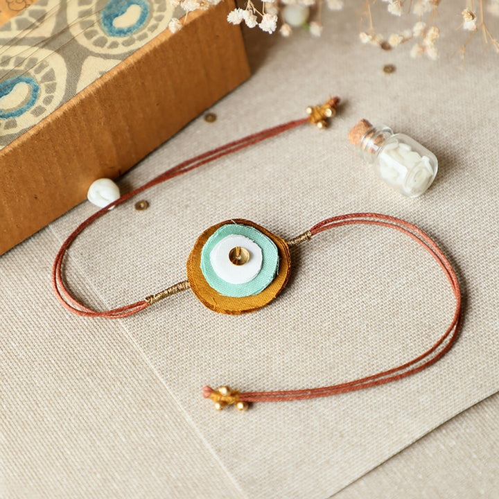 Handmade Reusable Layered Petal And Ghungroo Upcycled Fabric Rakhi With Roli Chawal For Brother - Front View with Bottle Prop