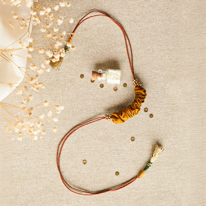 Handmade Reusable Gold Beads And Gathered Upcycled Fabric Rakhi With Roli Chawal For Brother - Flat Lay with Decorative Bottle