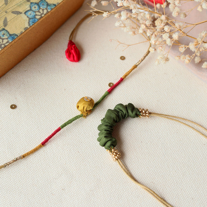 Handmade Reusable Pod And Gathered Upcycled Fabric Rakhi With Roli Chawal For Brother Set Of 2 - Flat lay showing two necklaces