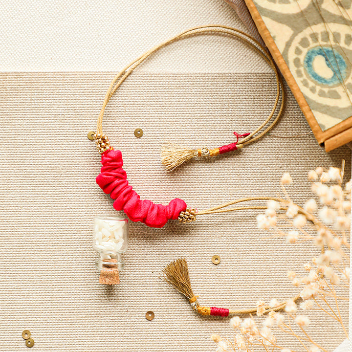 Handmade Reusable Gold Beads And Gathered Upcycled Fabric Rakhi With Roli Chawal For Brother - Flat Lay with Bottle Close-up