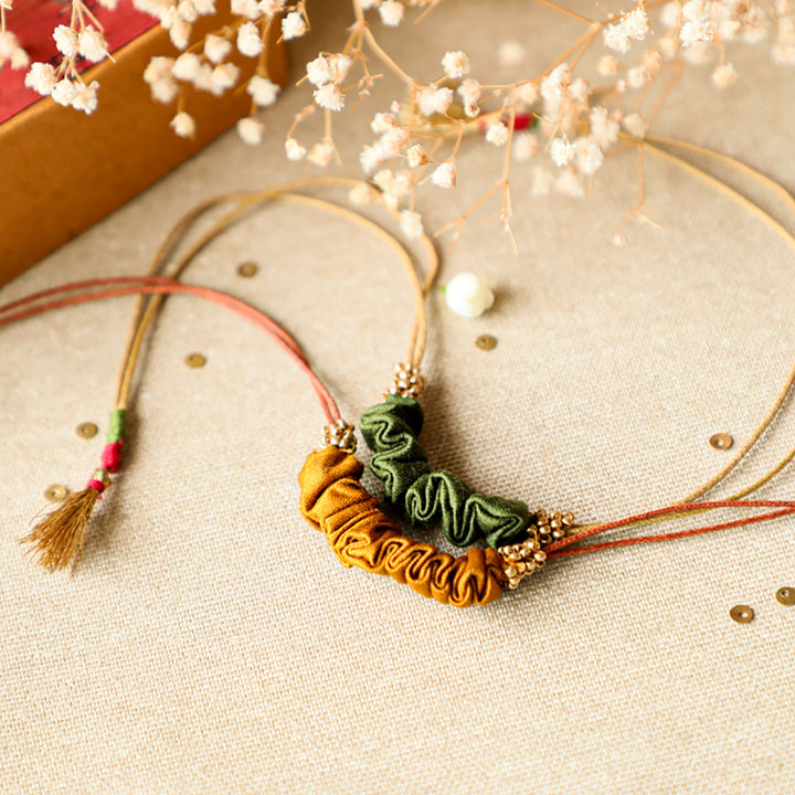 Handmade Reusable Gold Beads And Gathered Upcycled Fabric Rakhi With Roli Chawal For Brother Set Of 2 - Angled view with dried flowers