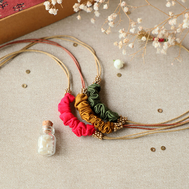 Handmade Reusable Gold Beads And Gathered Upcycled Fabric Rakhi With Roli Chawal For Brother Set Of 3 - Styled Flat Lay with Necklace
