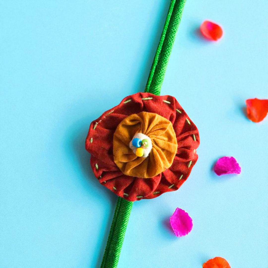 Handmade Brown And Orange Floral Upcycled Fabric Rakhi With Roli Chawal For Brother - Close-up View with Mixed Petals