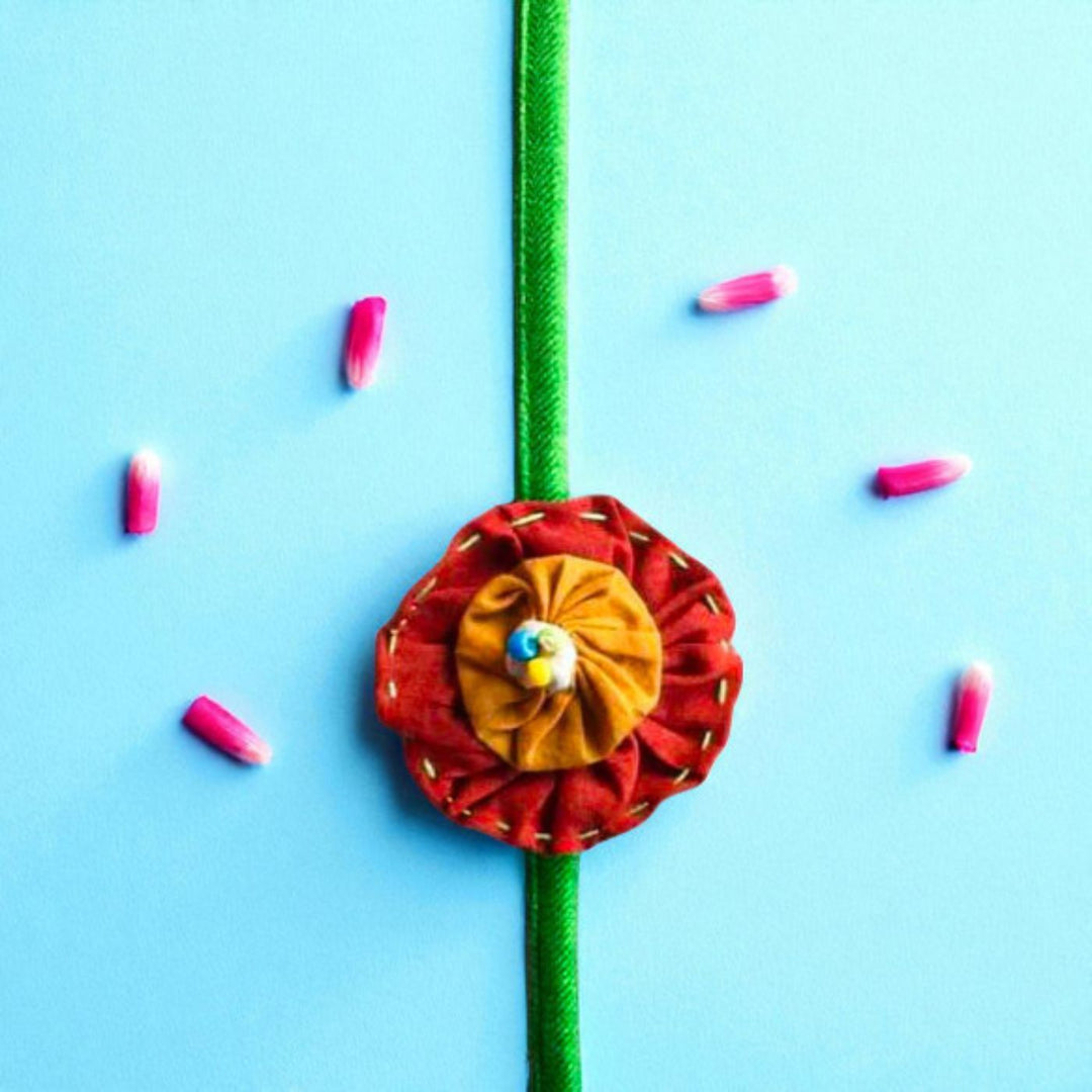 Handmade Brown And Orange Floral Upcycled Fabric Rakhi With Roli Chawal For Brother - Top View with Flower Decoration