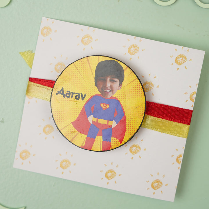 Photo Personalized Handmade Reusable Caricature Superman Mdf Wood Kids Rakhi With Roli Chawal - Badge on card flat lay