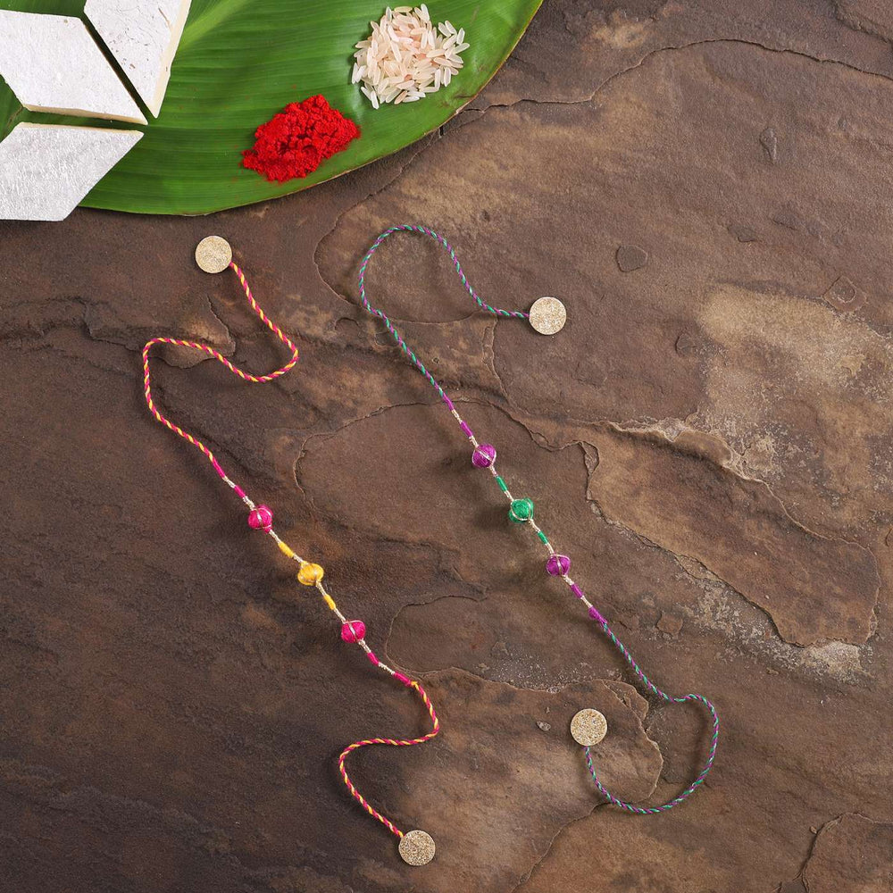 Handmade Zari Dori Fabric Rakhi With Roli Chawal Set Of 2 - Flat Lay on Textured Surface