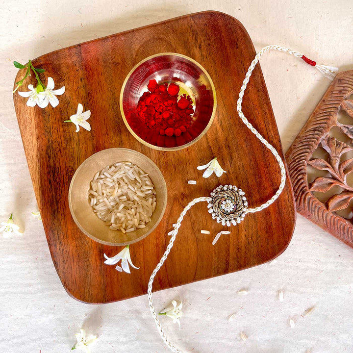 Handmade Zardozi White Bead Work Rakhi With Wooden Box And Roli Chawal - Flat lay with ritual items