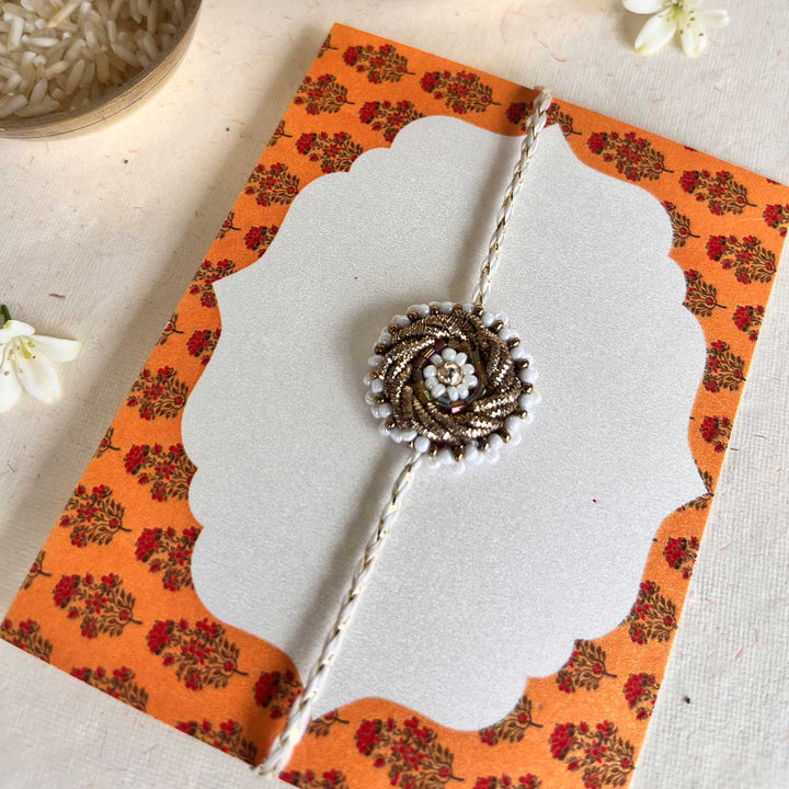 Handmade Zardozi White Bead Work Rakhi With Wooden Box And Roli Chawal - Packaging on patterned card