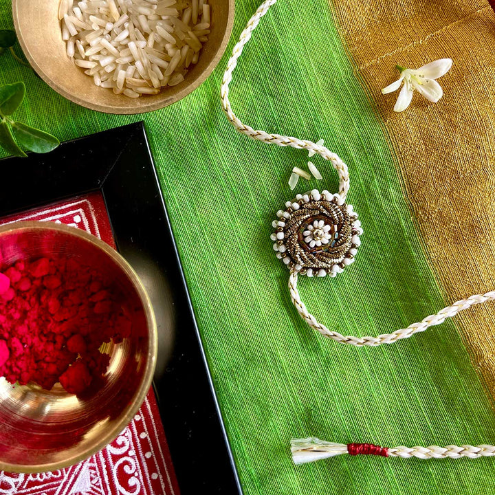 Handmade Zardozi White Bead Work Rakhi With Wooden Box And Roli Chawal - Styled with green fabric background