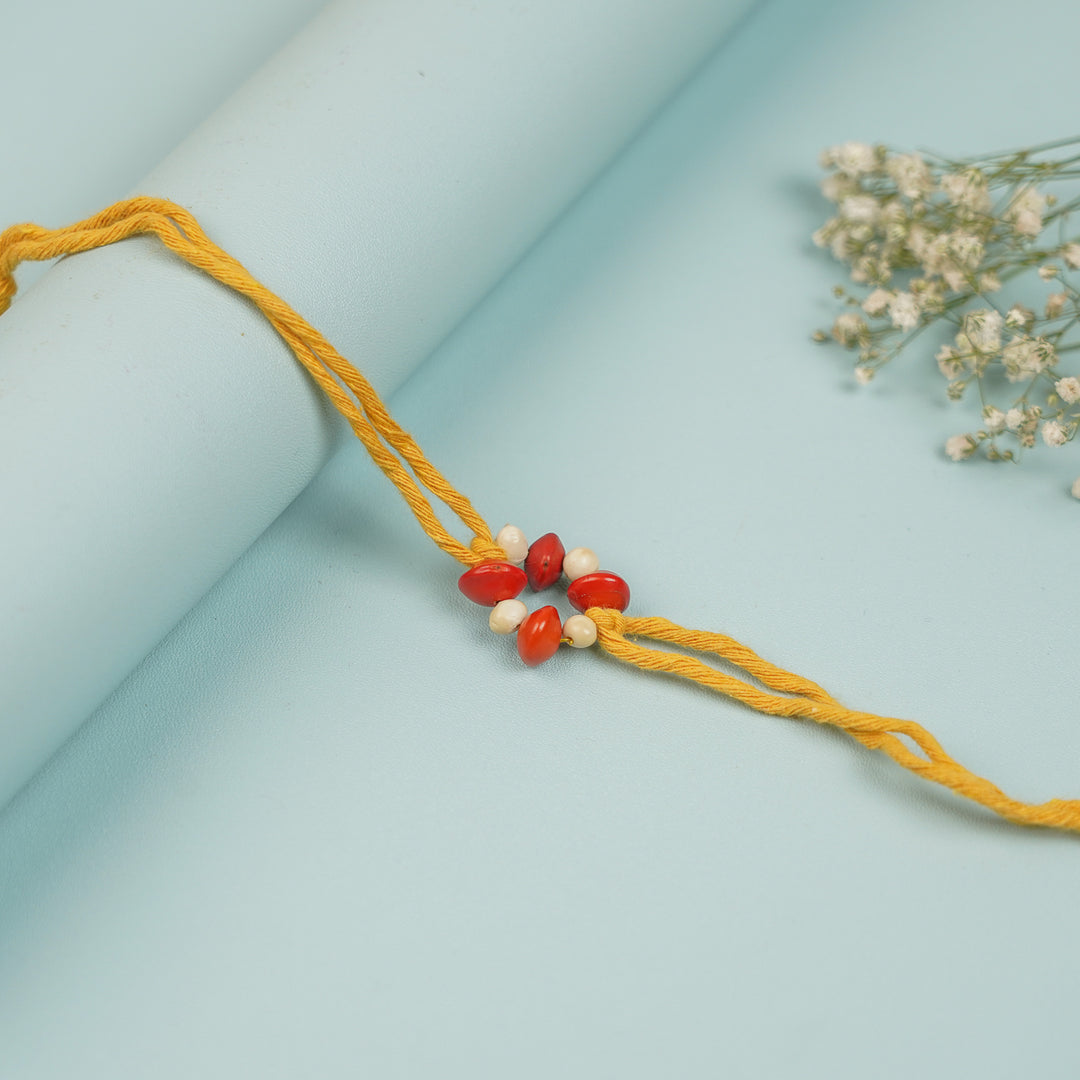 Handmade Red And White Gunj Flower Design Seed Rakhi For Brother - Full View of Bracelet on Surface