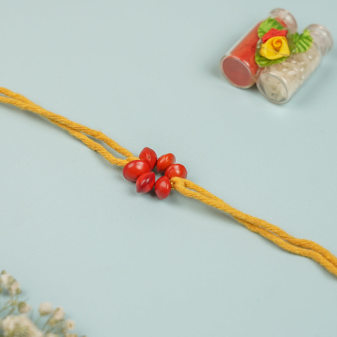 Handmade Red Gunj Flower Design Seed Rakhi For Brother - Flat lay showing full string length