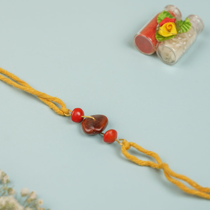 Handmade Tamarind Red Gunj Design Seed Rakhi For Brother - Flat Lay with Decorative Bottles