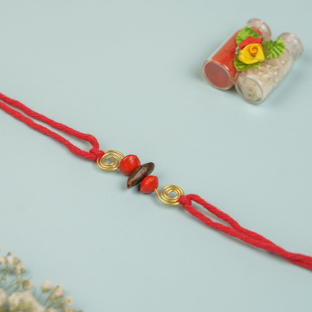 Handmade Tamarind Spiral Sitaphal Red Gunj Design Seed Rakhi For Brother - Flat Lay with Decorative Bottles