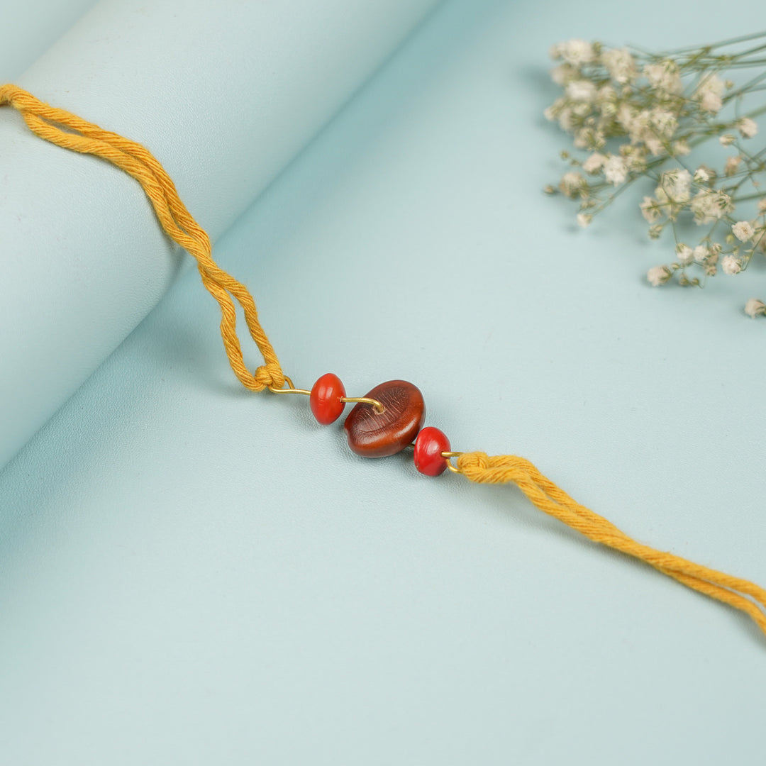 Handmade Tamarind Red Gunj Design Seed Rakhi For Brother - Close-up Flat Lay with Flowers