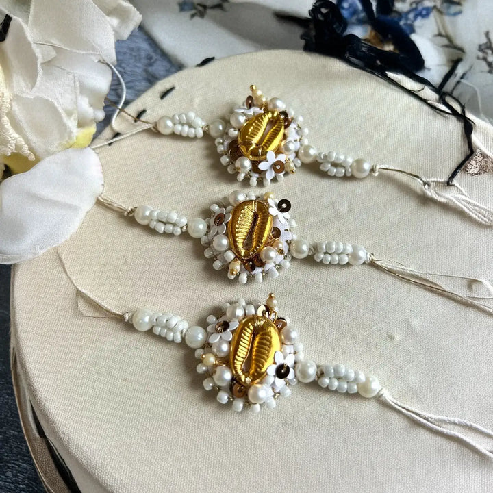 Hand Embroidered Beaded White And Golden Shell Rakhi With Roli Chawal Set Of 3 - Three Bracelets Laid on Round Surface