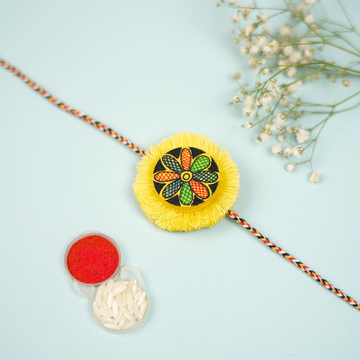 Hand Painted Madhubani Yellow Flower Design Wooden Rakhi With Roli Chawal For Brother - Flat Lay with Haldi Rice Containers