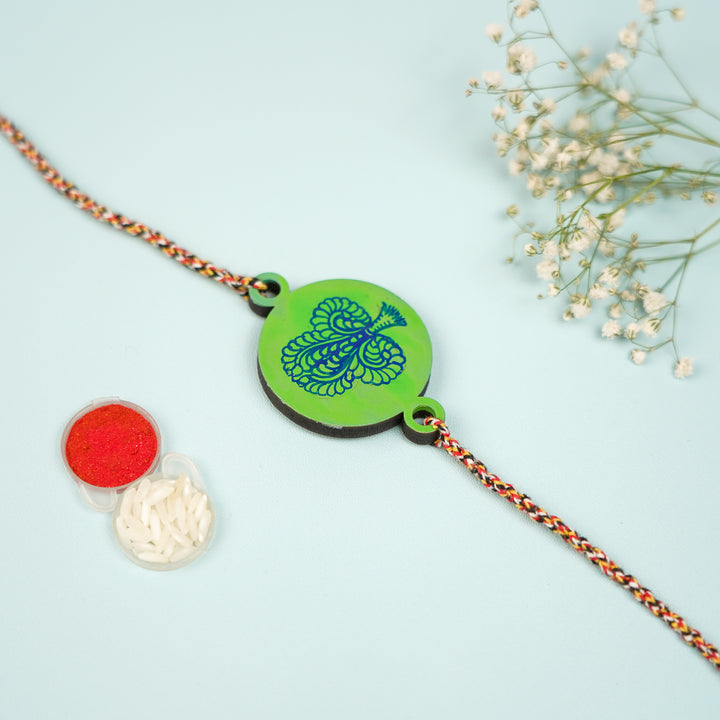Hand Painted Pattachitra Peacock Feather Design Wooden Rakhi With Roli Chawal For Brother - Close-up with rice and kumkum