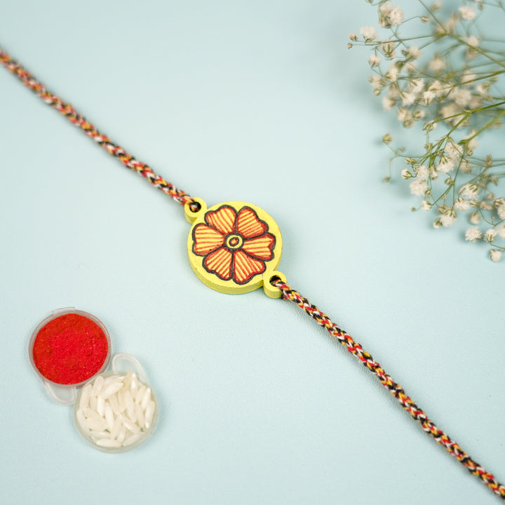 Hand Painted Madhubani Yellow Flower Design And Beads Wooden Rakhi With Roli Chawal For Brother - Flat Lay with Rice and Red Powder