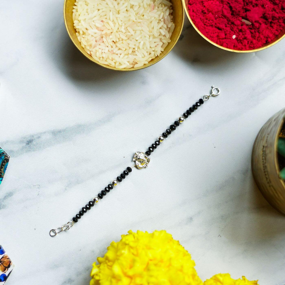 Handcrafted Nazar Battu Silver Ganesha Rakhi For Newborns With Rice Roli - Flat Lay with Themed Accessories