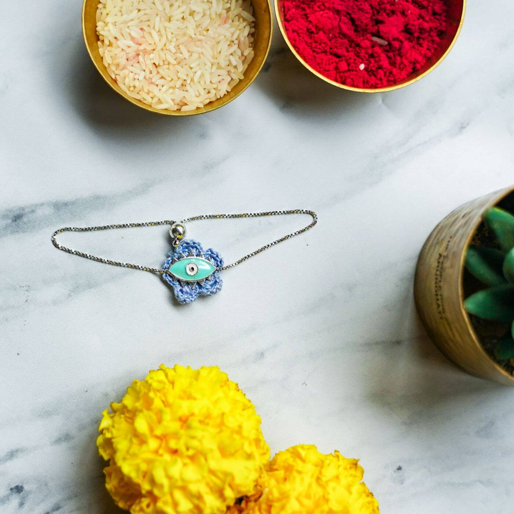 Handcrafted Evil Eye Silver Strap Rakhi For Kids With Rice Roli - Flat Lay with Decorative Items