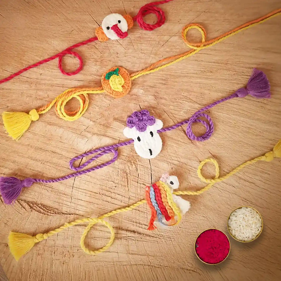 Handmade Crochet Ganesha Mango Sheep And Unicorn Kids Rakhi With Roli Chawal Set Of 4 - Laid Flat with Puja Ingredients