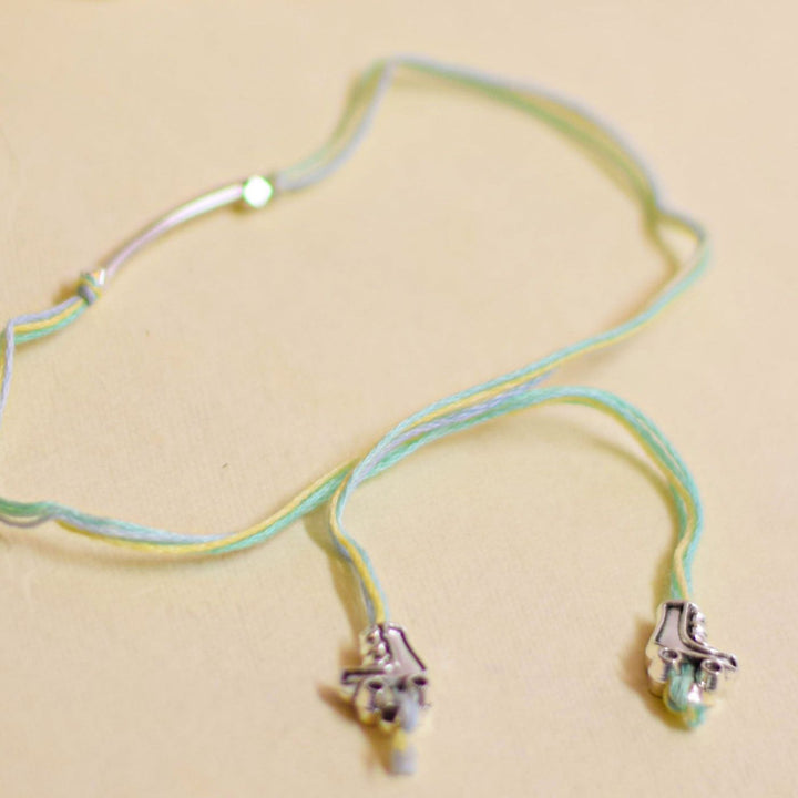 Handmade Stake Board Shoe And Pearl Design Rakhi With Roli Chawal - Green and yellow bracelet flat lay
