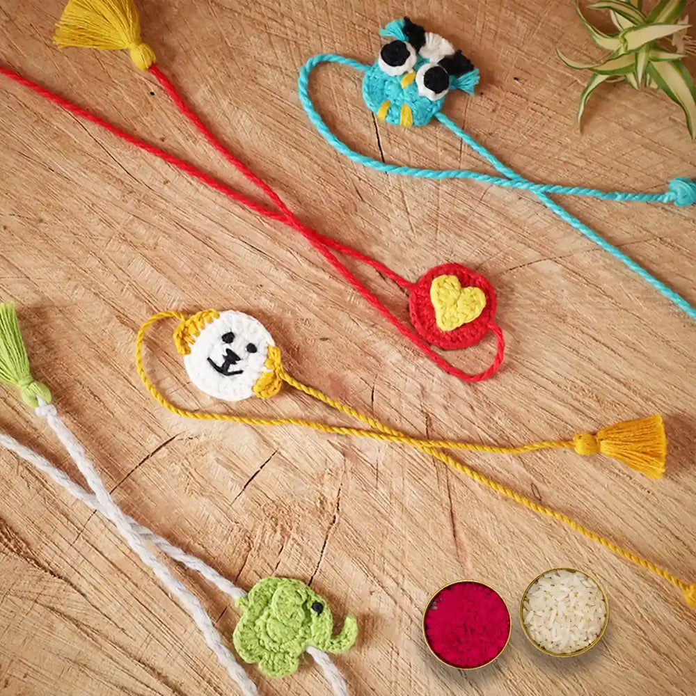 Handmade Crochet Owl Elephant Dog And Heart Kids Rakhi With Roli Chawal Set Of 4 - Laid Out on Wooden Surface