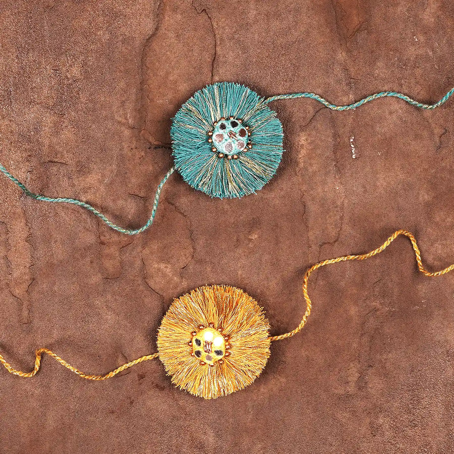 Handmade Mirror Work Blue And Yellow Rakhi With Roli Chawal Set Of 2 - Lying Flat on Textured Surface
