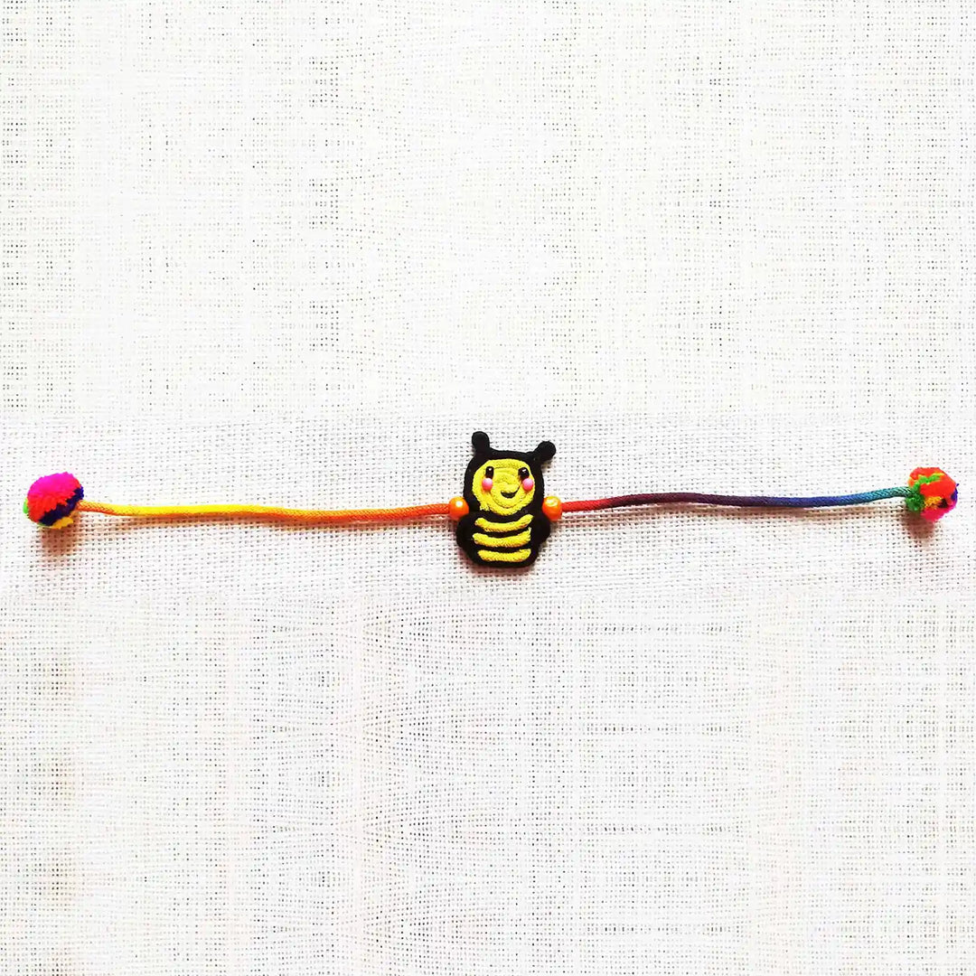 Handmade Dori Work Cute Bumble Bee Kids Rakhi With Roli Chawal - Laid Flat on Fabric Background