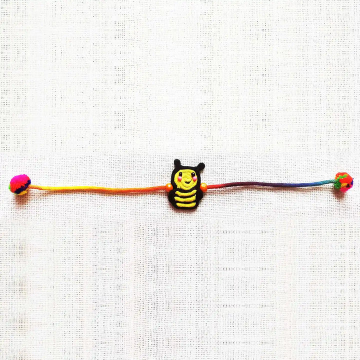 Handmade Dori Work Cute Bumble Bee Kids Rakhi With Roli Chawal - Laid Flat on Fabric Background