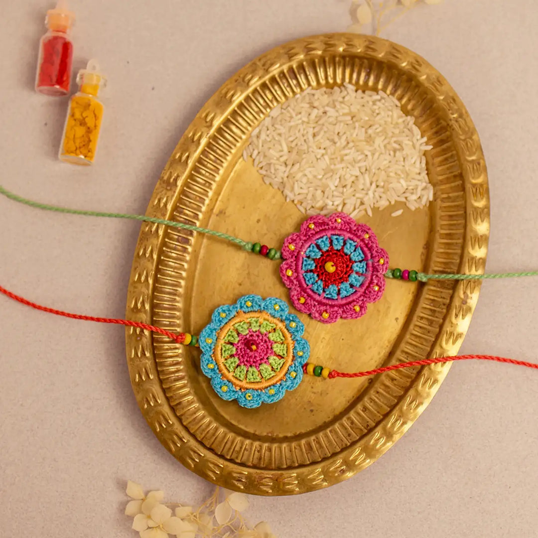 Handmade Crochet Floral Noor Rakhi With Roli Chawal Set Of 2 - Front View on Brass Tray
