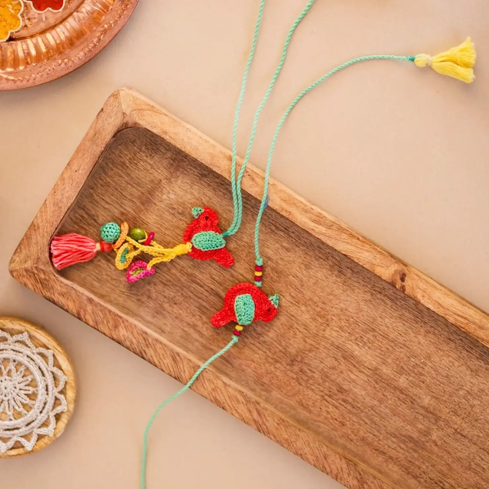 Handmade Crochet Birds Bhaiya Bhabhi Rakhi With Roli Chawal Set Of 2 - Angled View with Wooden Tray
