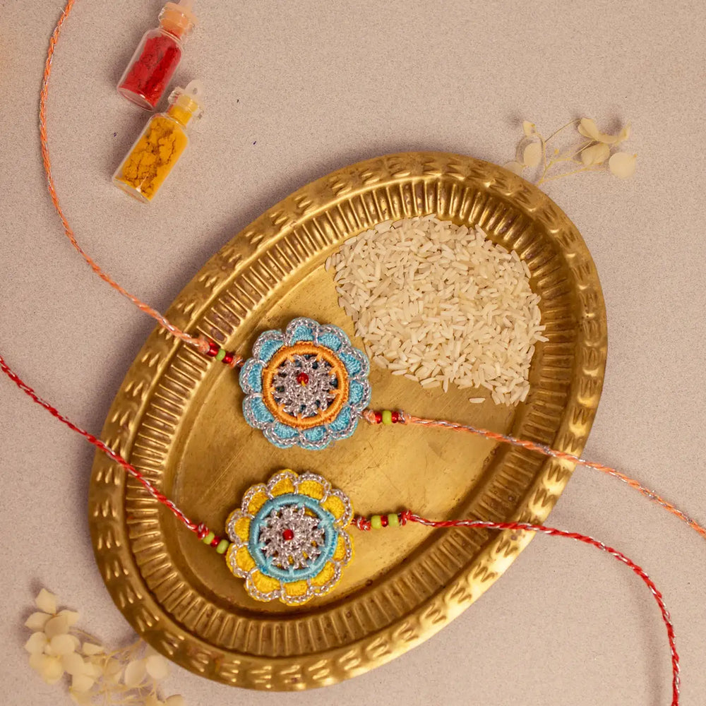 Handmade Crochet Palash Rakhi With Roli Chawal Set Of 2 - Flat Lay with Plate and Rice