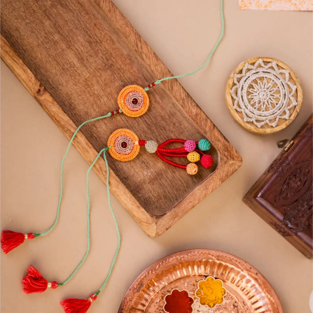 Handmade Crochet Kesaria Mandala Bhaiya Bhabhi Rakhi With Roli Chawal Set Of 2 - Styled Flat Lay with Accessories