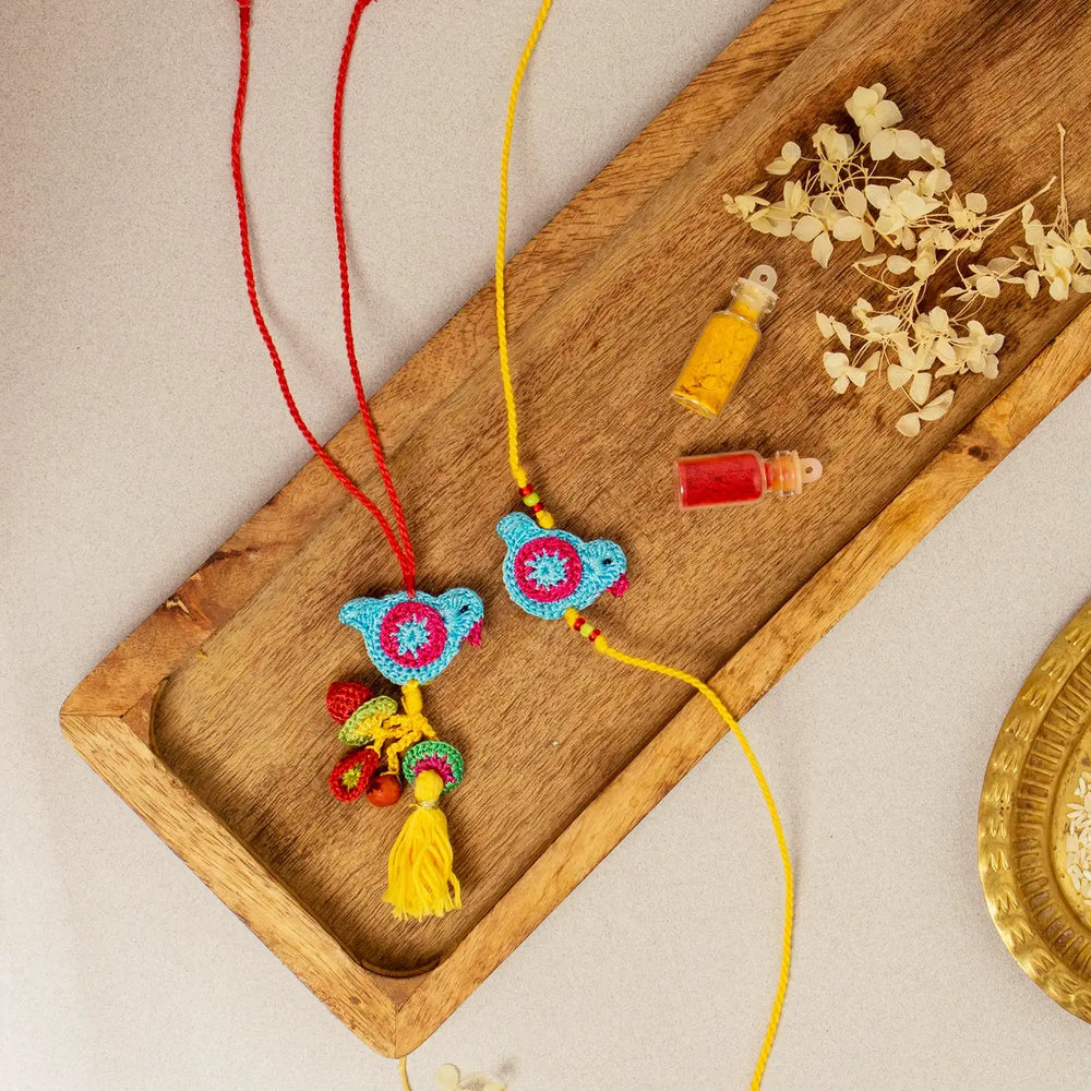 Handmade Crochet Blue Birds Bhaiya Bhabhi Rakhi With Roli Chawal Set Of 2 - Flat lay on wooden tray