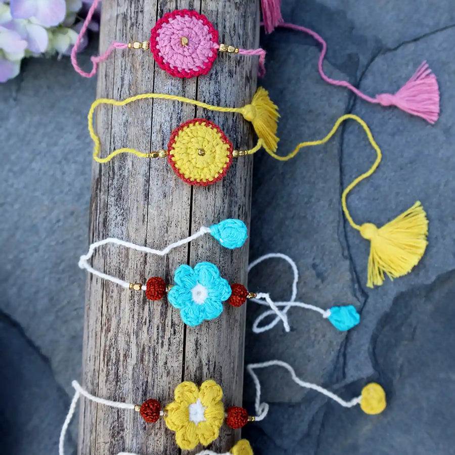 Handmade Crochet Pink Yellow And Blue Rudraksh Rakhi With Roli Chawal Set Of 4 - Laid on wooden log close-up