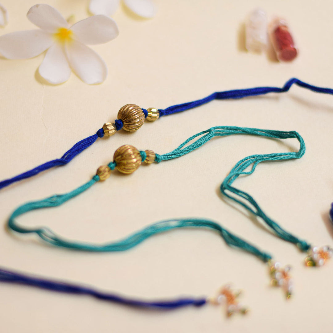 Handmade Swarn Pearl And Ghungroo Rakhi With Roli Chawal - Pair arrangement on beige background