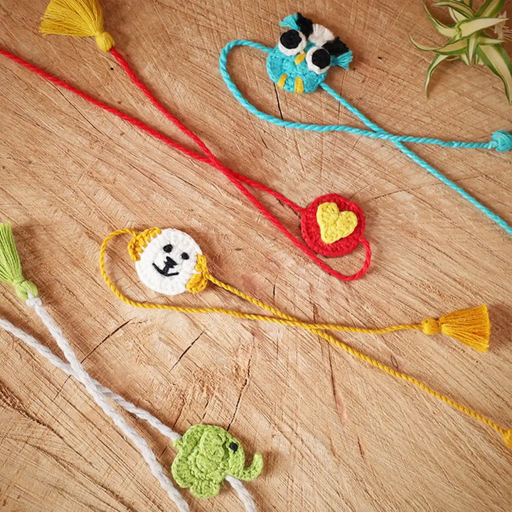 Handmade Crochet Owl Elephant Dog And Heart Kids Rakhi With Roli Chawal Set Of 4 - Laid Out on Wooden Surface (4)