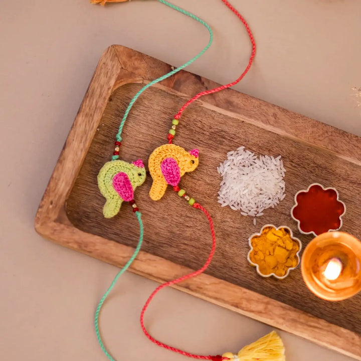 Handmade Crochet Yellow And Green Chidiya Rakhi With Roli Chawal Set Of 2 - Flat Lay Showing Full Length Strings