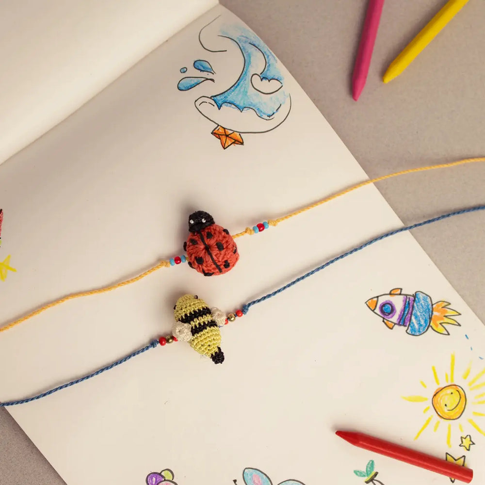 Handmade Crochet Beetle And Bee Theme Kids Rakhi With Roli Chawal Set Of 2 - Top View on Illustrated Background