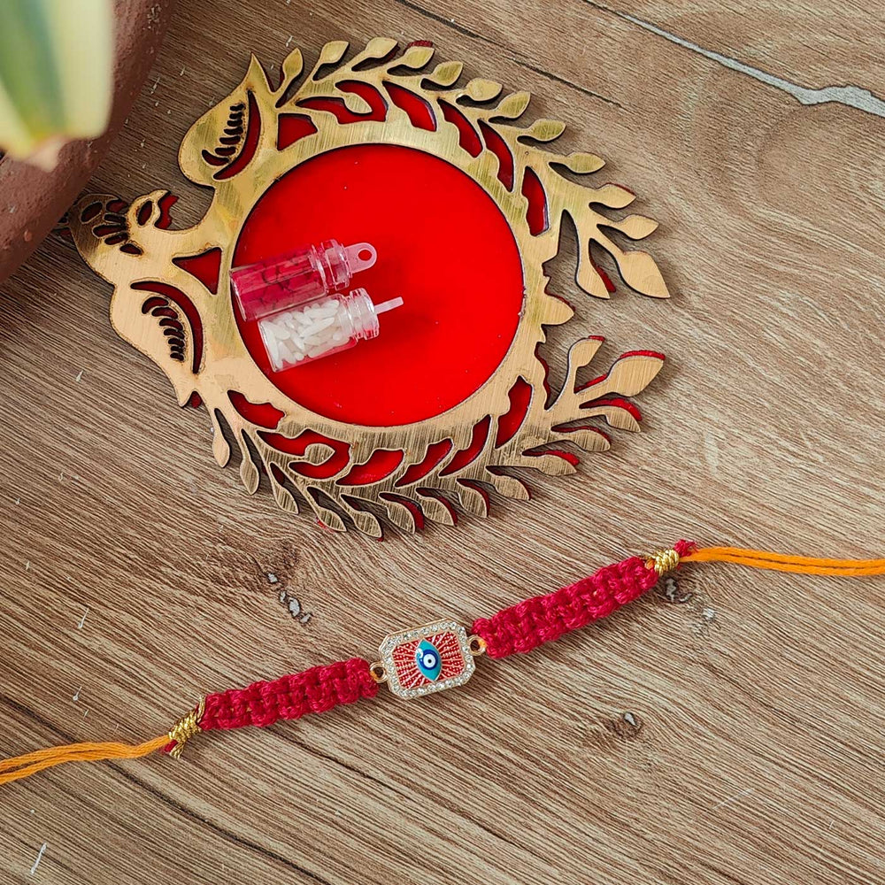 Handmade Macrame Brown Evil Eye Metal Rakhi With Roli Chawal - Full product with decorative plate background